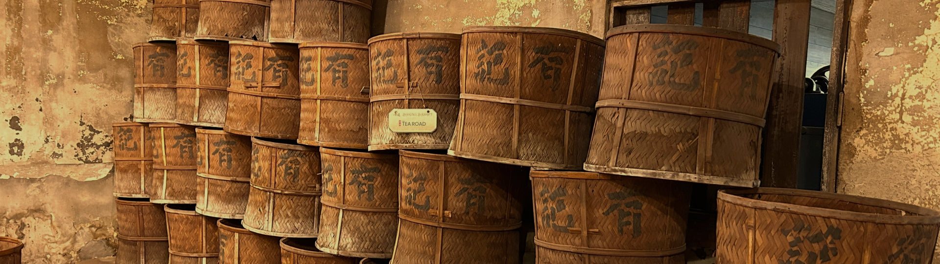 Row of bamboo tea roasting barrels against a textured wall.
