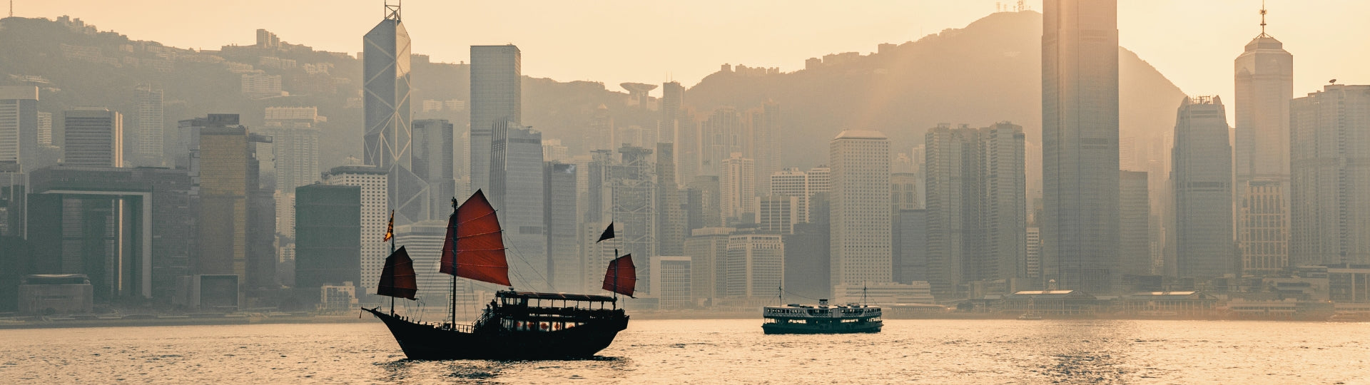 Traditional Chinese junk ship sailing on Victoria Bay with Hong Kong skyline in the background