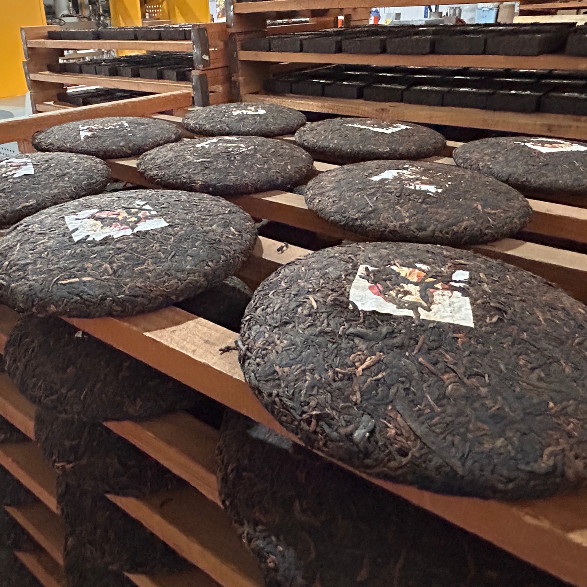 Stacks of compressed tea cakes on wooden shelves with labels