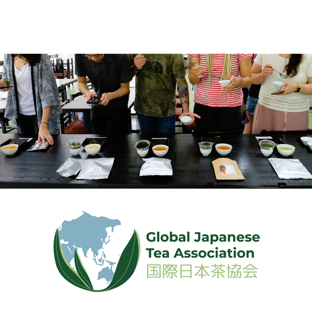 Tea tasting event with participants and tea samples on a table and the Global Japanese Tea Association logo underneath