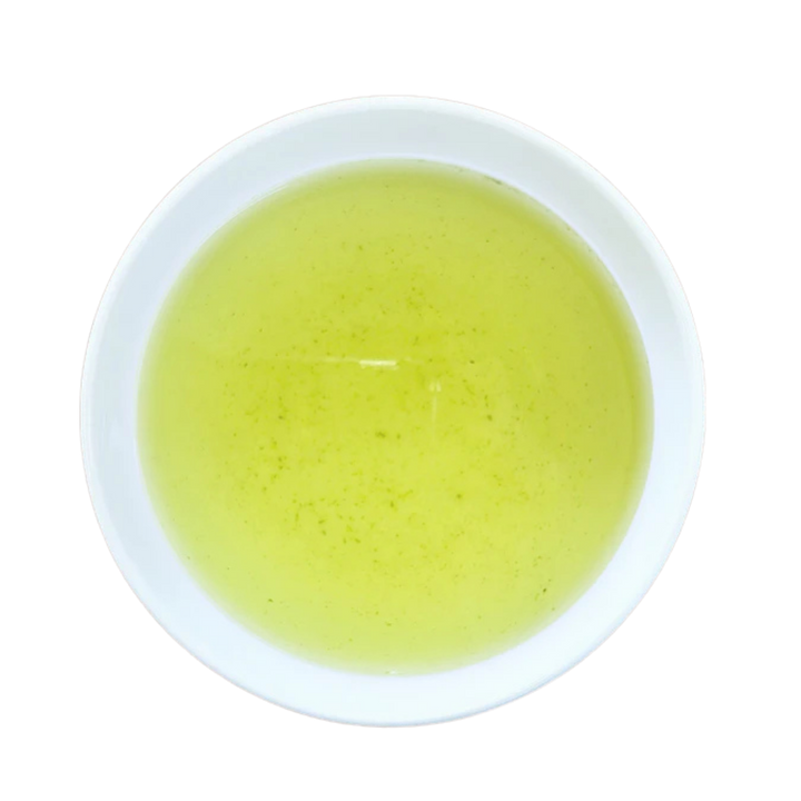 A top-down view of a light yellow-green tea presented in a white ceramic bowl