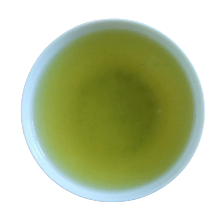 A top-down view of a white cup filled with light yellow-green tea