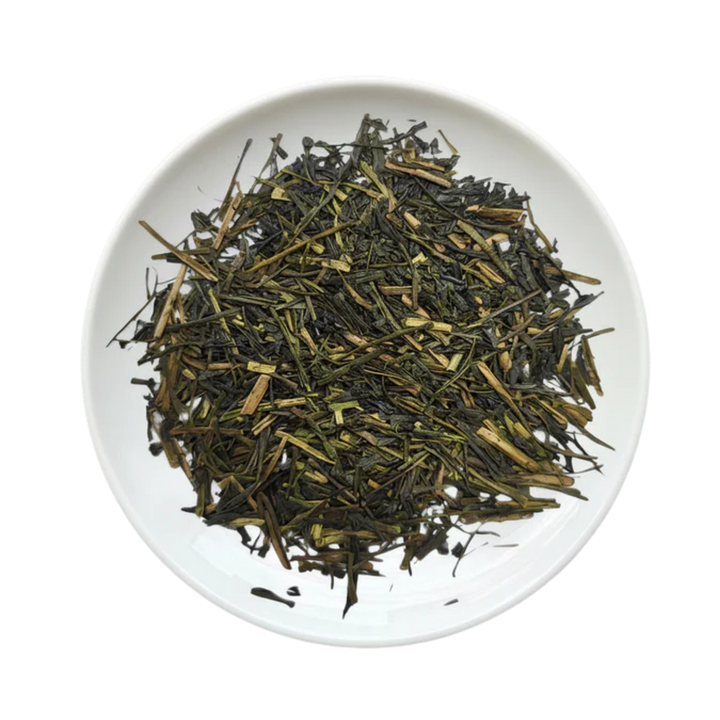 A top-down view of loose-leaf tea leaves, showing dark green and light brown needles, presented in a white ceramic plate