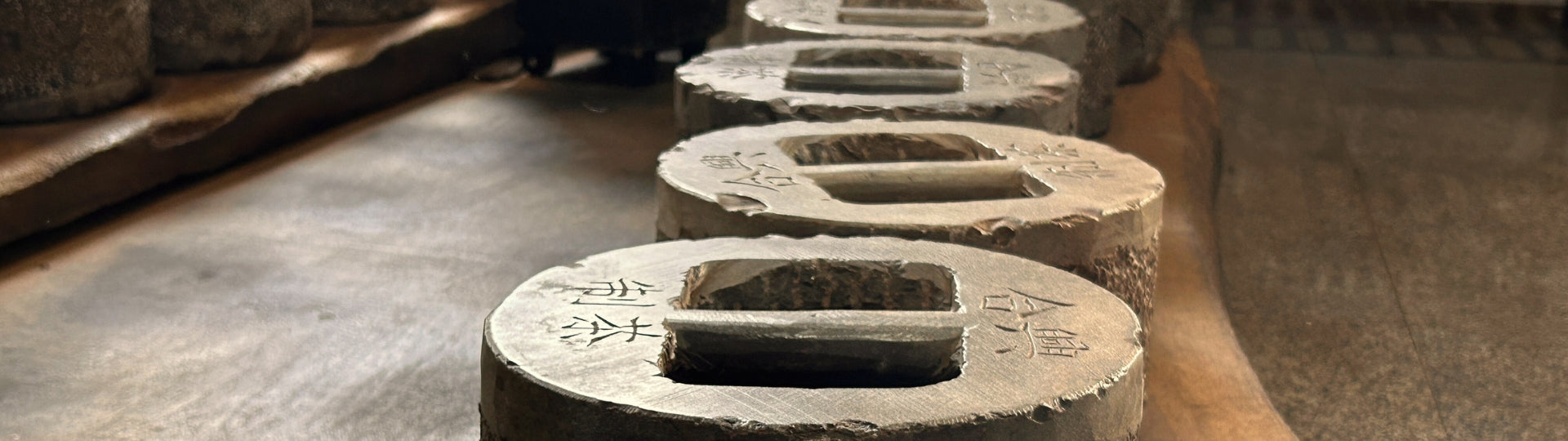 Row of tea cake pressing stone with engraved kanji signs on a wooden plate