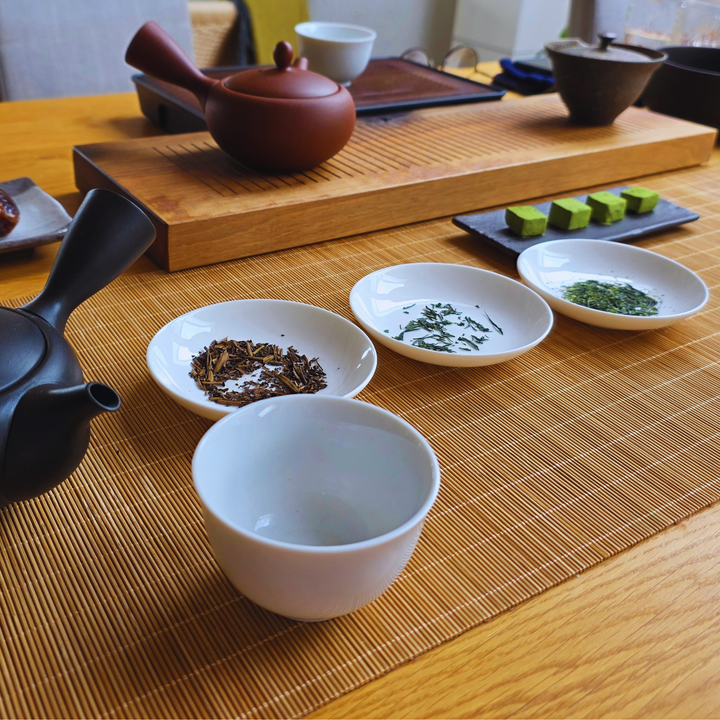 A tea table setup with 2 kyusus, a white ceramic cup and some small ceramic trays with tea leaves
