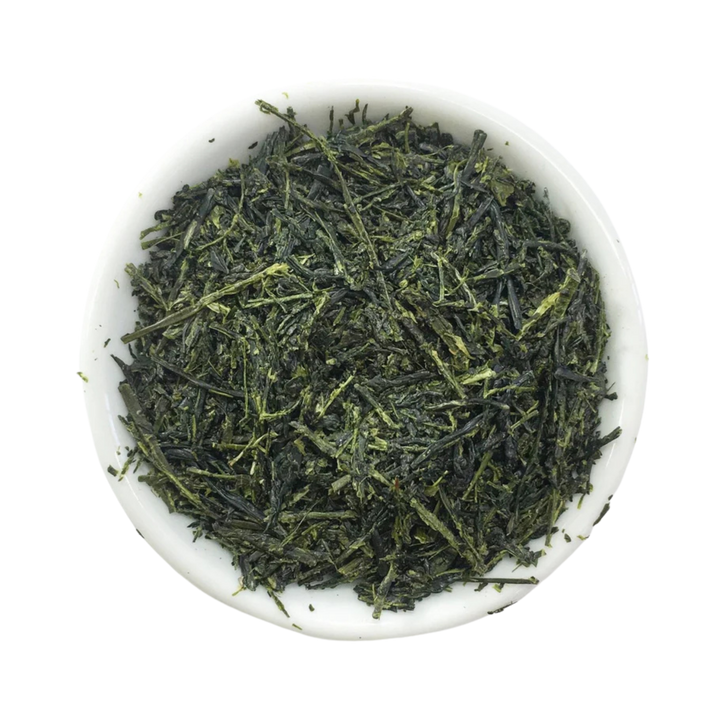 Dried loose-leaf green tea leaves piled in a small white ceramic bowl  photographed from above
