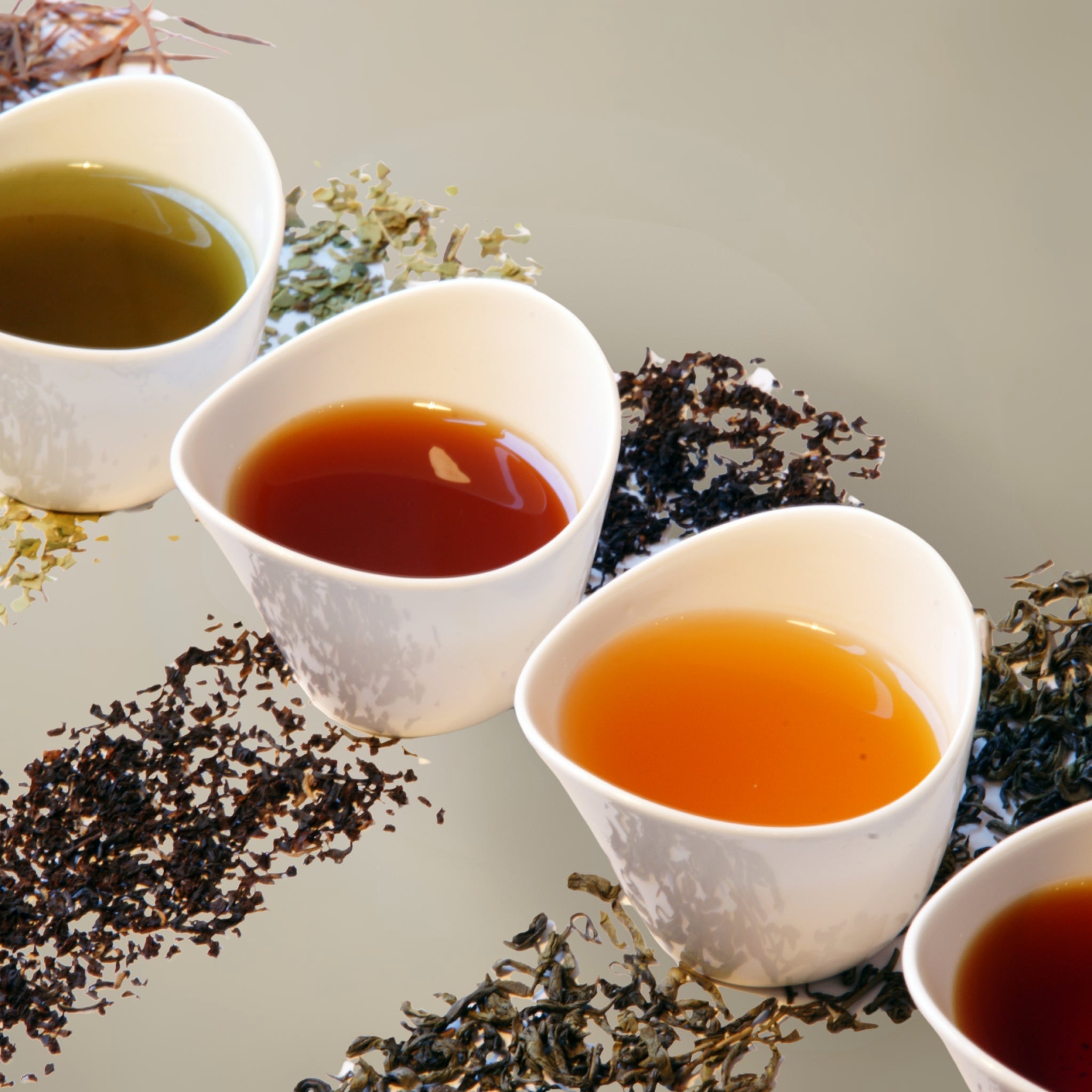 Three white cups filled with different types of tea, surrounded by tea leaves on a light background