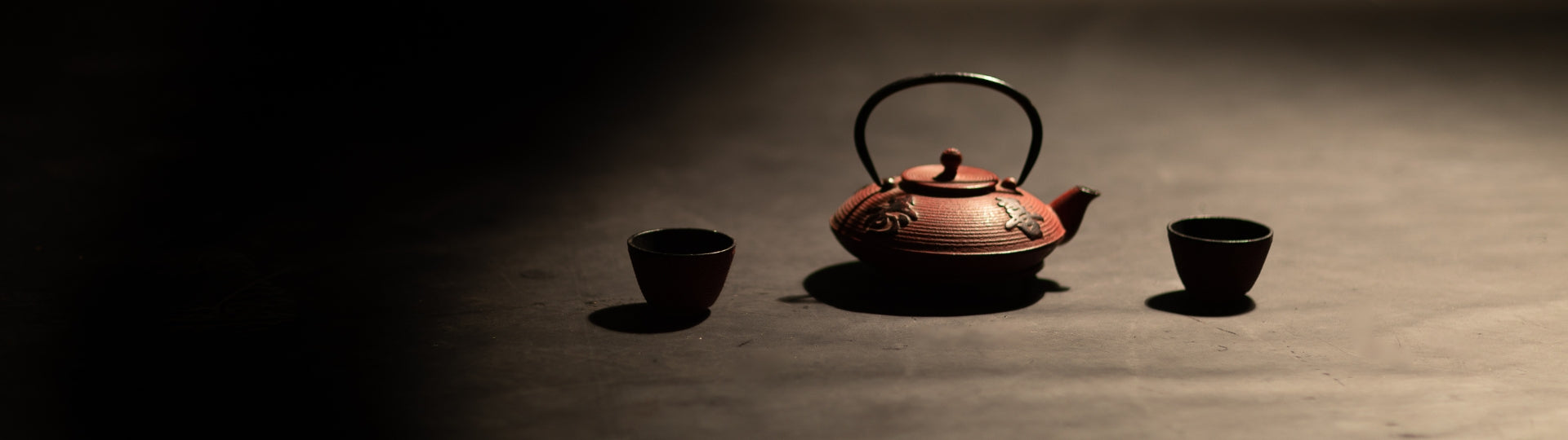 Traditional Chinese iron teapot with two cups on a dark grey surface
