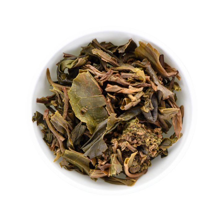Green and light-brown tea leaves in a white porcelain cup