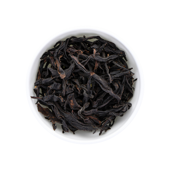 Dark dried tea leaves filling a small white round bowl, photographed from above