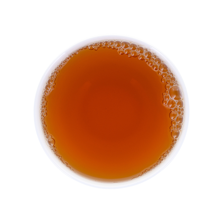 A top-down view of a white cup filled with amber-brown tea, showing a layer of bubbles around the rim