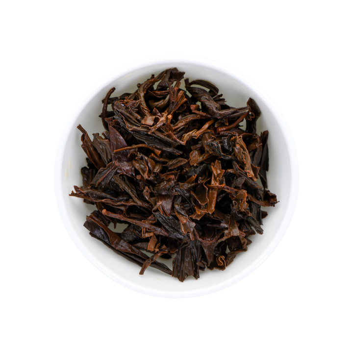 Dark brown wet tea leaves piled in a small white ceramic bowl, photographed from a top-down view